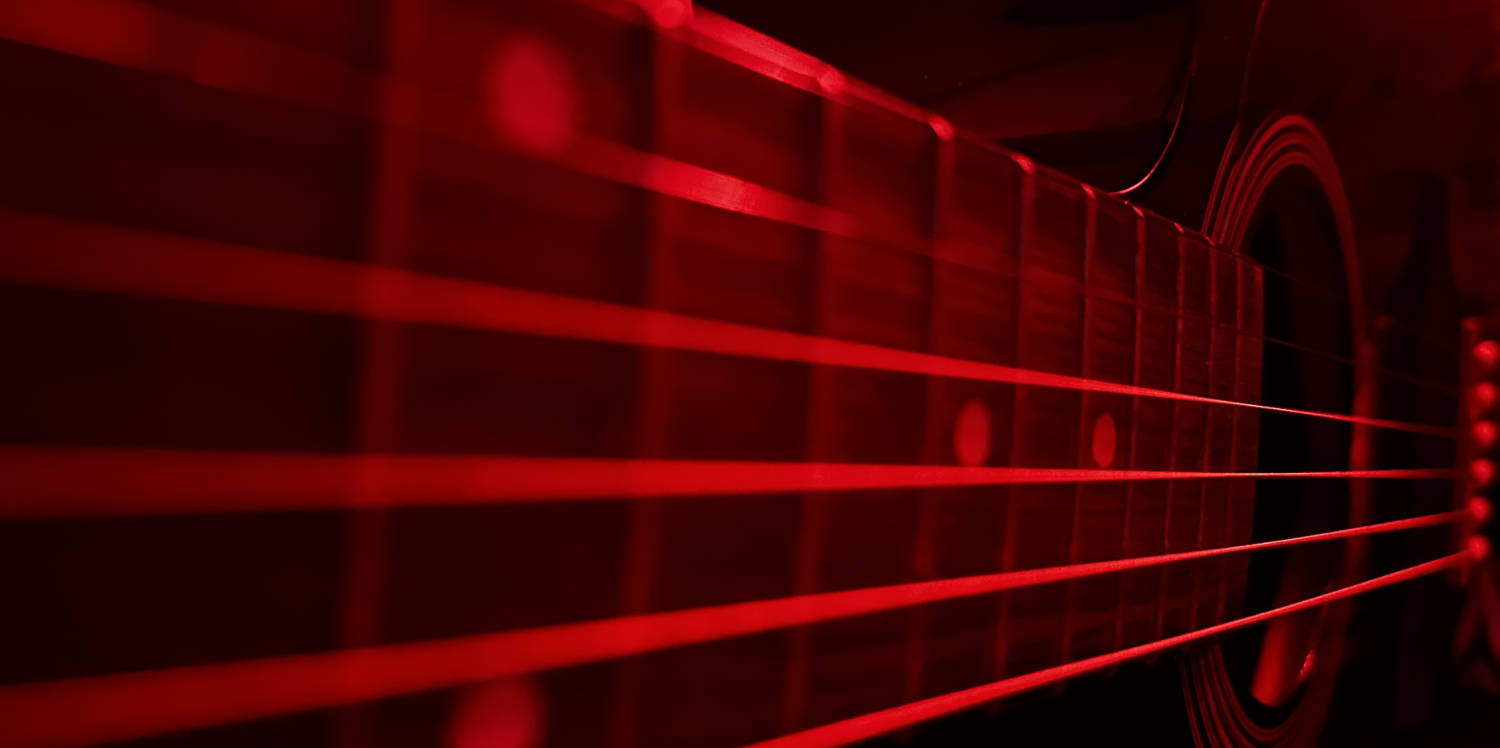 Close up photo of strings of a guitar in red lighting