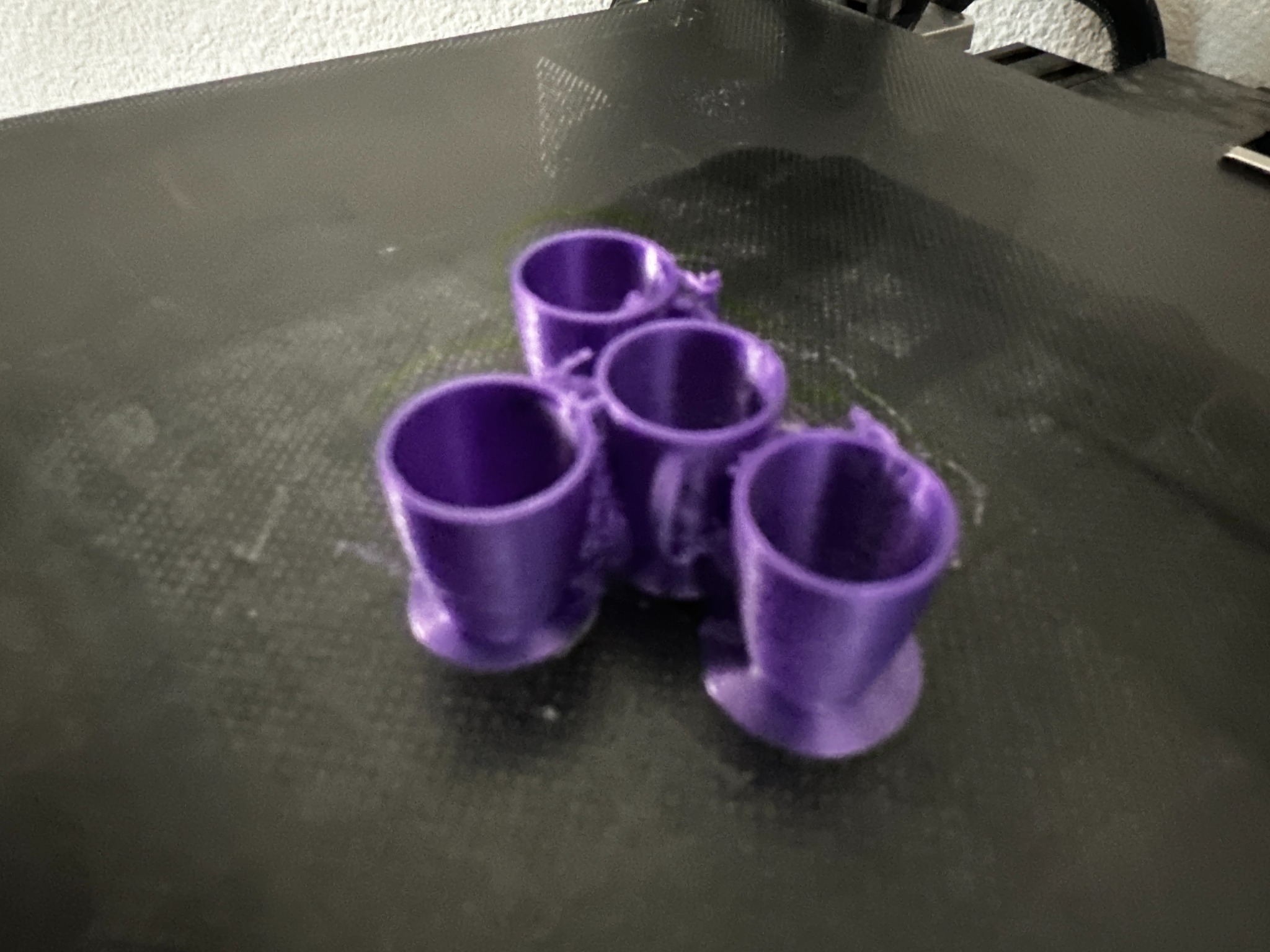 Four tiny cup-shaped test prints on the 3D printer bed