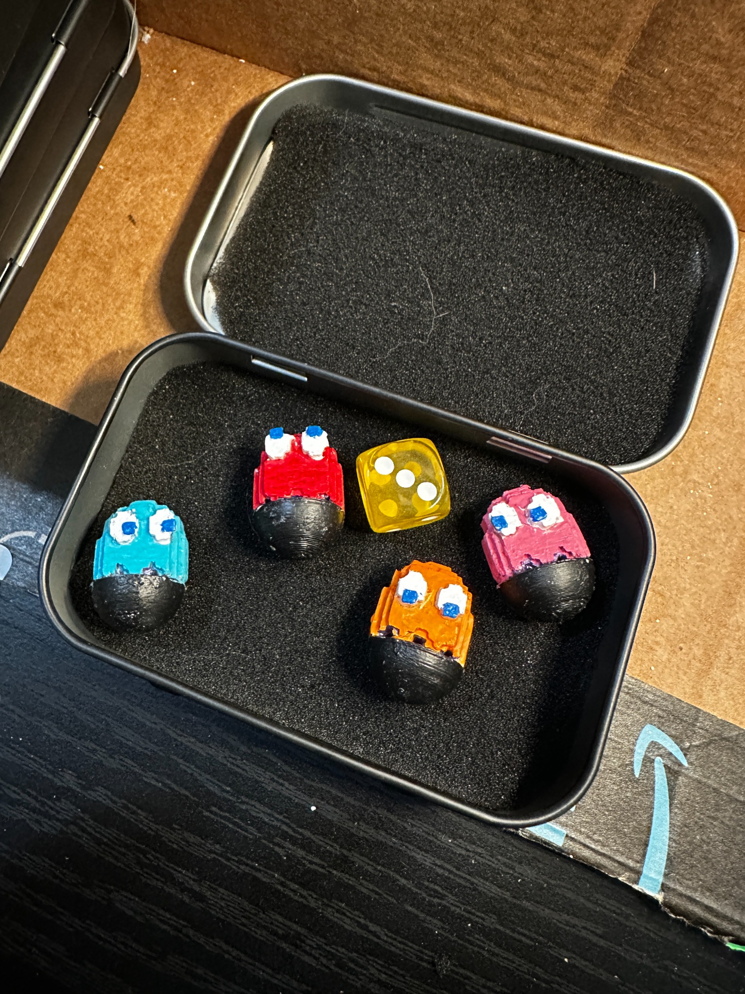 Metal gift tin with black foam insert holding ghost marble set and die